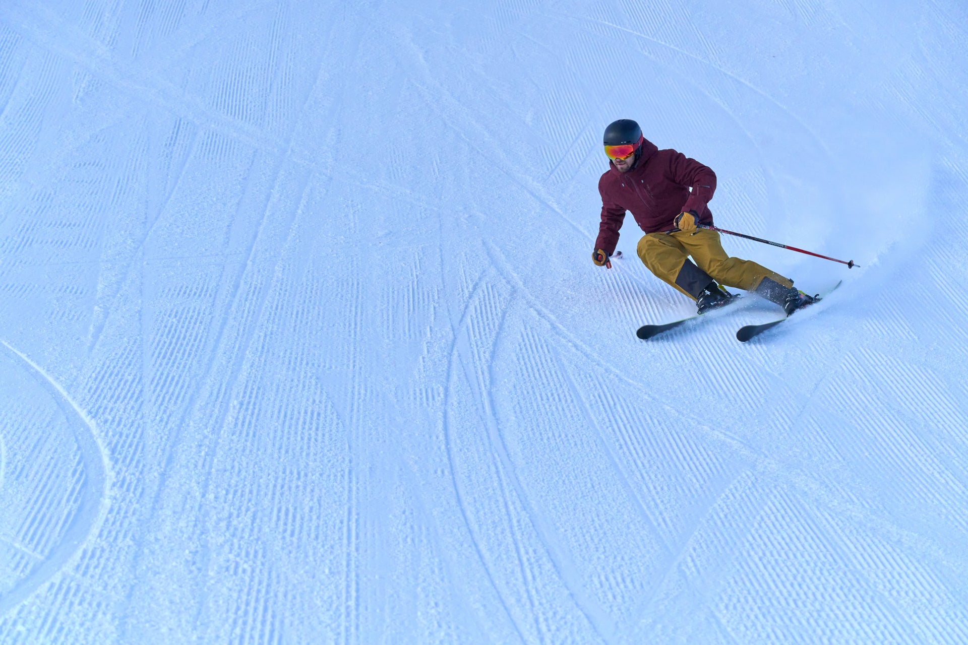 Untrakt | A skier in a maroon jacket and yellow pants making a turn on a groomed slope